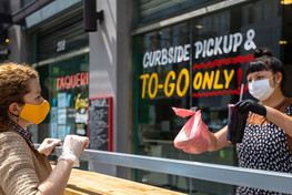 Masked restaurant worker outside handing masked customer a to-go order