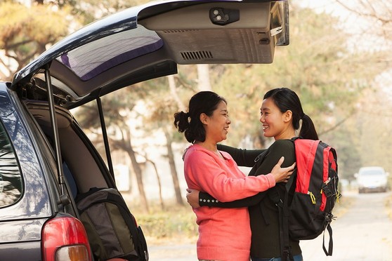 A young adult shares an embrace with her mother as she packs her car.