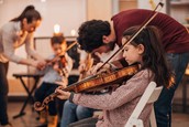 Photo of two adult tutors giving violin lessons to two children