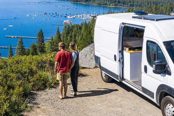 A couple holds hands outside of their parked RV as they take in a scenic view.