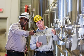 Two workers at a manufacturing plant review their notes on a project. 