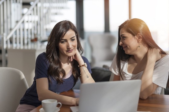 Two women sit together at a table in their apartment.