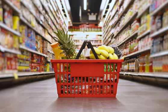 A basket full of groceries sits on the ground in the middle of a supermarket aisle.