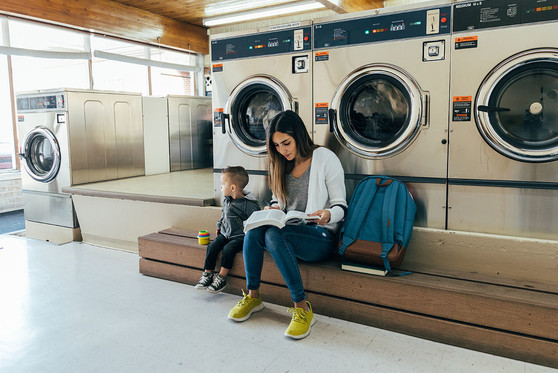 A mother and her son wait for their clothes to finish washing at a laundromat.