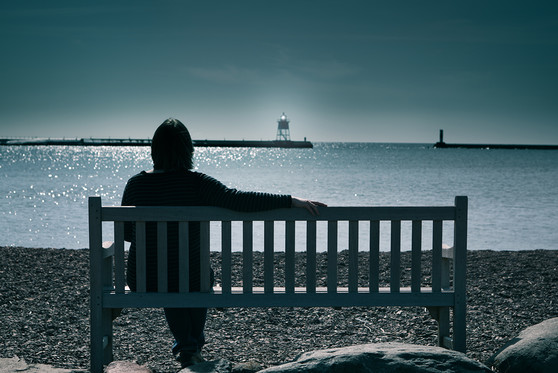 A woman sits at a bench overlooking a body of water.