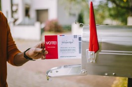A person puts a completed election ballot into their mailbox.