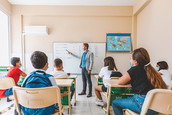 A teacher wearing a face mask lectures to his class.