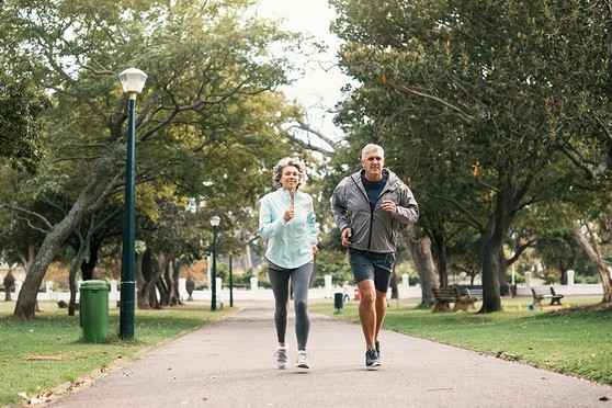 An older man and woman jog through a park.