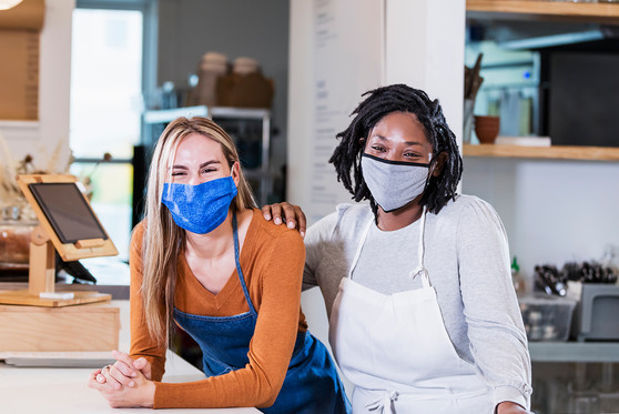 Two female workers with face masks on pose together behind a restaurant counter.