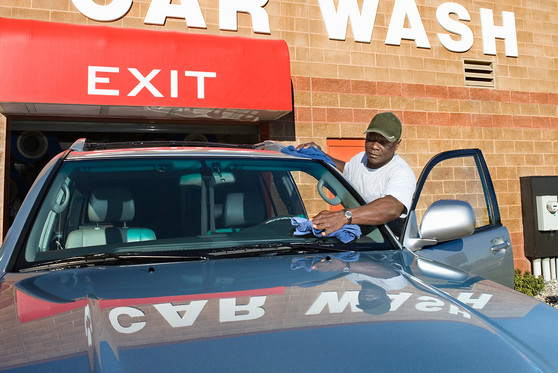 A man washes the windshield of a car at a car wash.