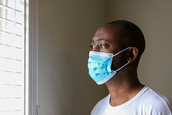 An African-American man looks out through a window in his residence.