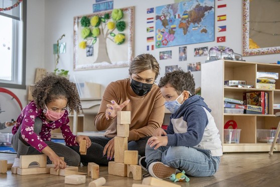 A mother actively engages her children while they play with building blocks.