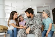 A veteran of the armed forces sits down on a couch with his wife and kids.