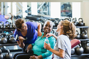 Three women chat while working out at a fitness center.