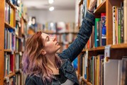 A woman reaches for a book on a high shelf at a bookstore.