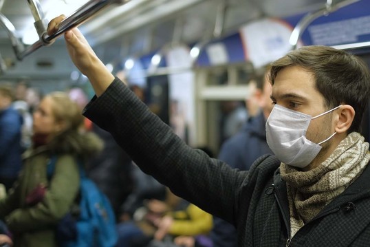 A man wearing a face mask on a subway train stands up and waits to get off at his stop.