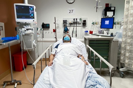 A patient laying in a hospital bed with an IV and monitor hooked up to them.