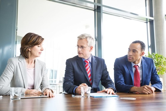 A woman sits with two men at a business meeting.