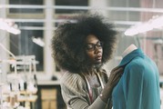 An African American woman puts a shirt on a mannequin in a stockroom.