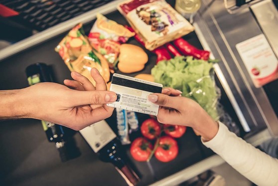 A customer hands a credit card to an employee at a market to purchase various foods and beverages.