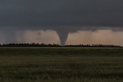 A funnel cloud appears over a grassy area.