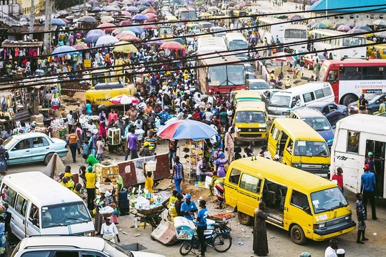 Crowds of people and vehicles gather around outdoor kiosks.