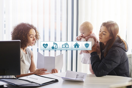 A mother sits with her baby daughter and meets with a woman to inquire about social safety net programs.