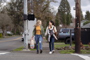 Two women with a baby walk down a street while holding hands.