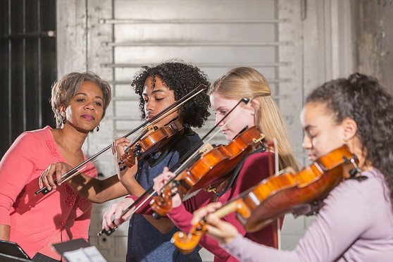 A music teacher looks on as her students practice playing violin.