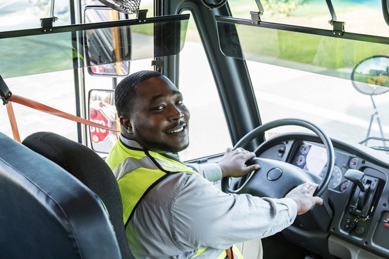 An African-American school bus driver sits in the driver's seat of a bus.