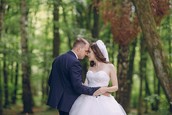 A bride and groom look at each other while standing in a wooded area.