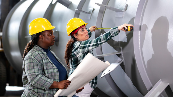 Female workers measure a large cylinder.