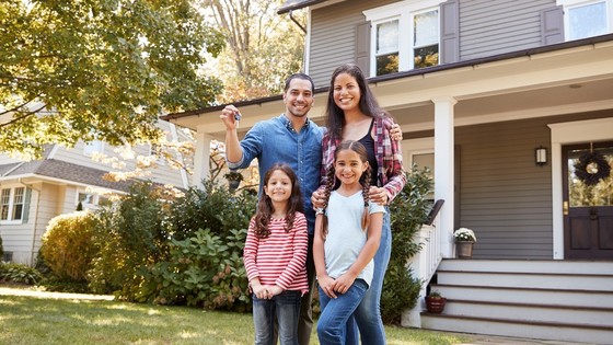 A family of four stands in front of their single family house.