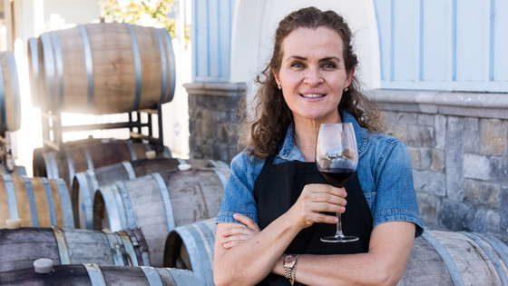 A woman holding a wine glass and standing in front of wine barrels