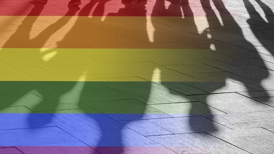 Shadows of people over a rainbow flag design painted on the ground