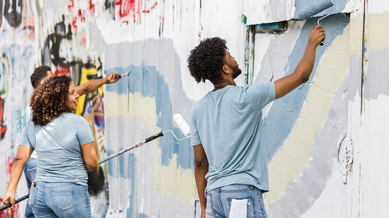 Volunteers work to paint over a wall of graffiti in a park.