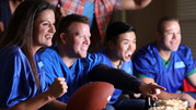 A group of people sit together to watch a football game on TV.