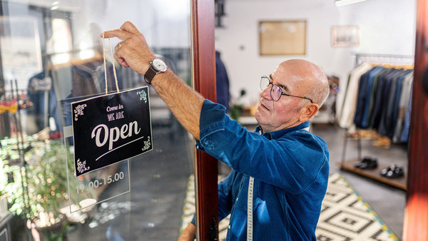 A male shop worker hangs a 'We are open' sign in  his shop.