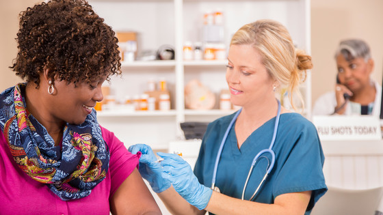 A nurse administers a vaccine to an African American woman at a clinic.