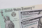 A U.S. Treasury-issued Economic Impact Payment lies under a pile of $100 bills.