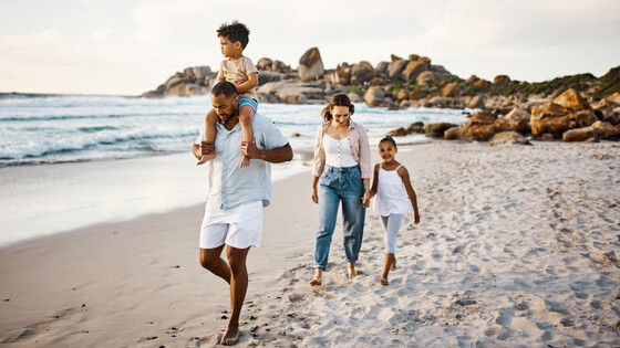 A family walks on the sand at a beach, very close to the water.