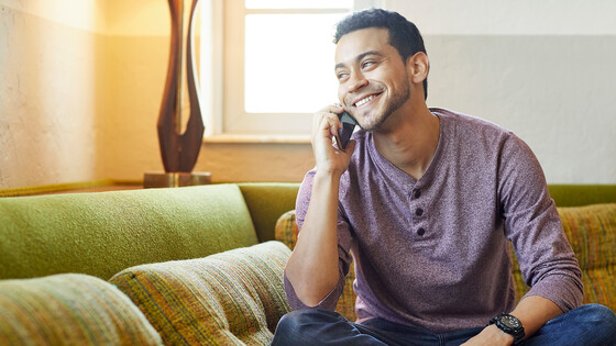 A man sits on his couch while talking on his mobile phone.