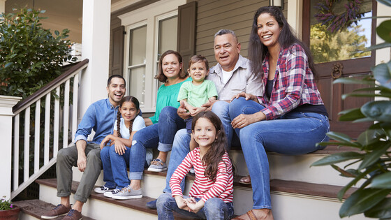 A multigenerational family sits on the front steps of their house.