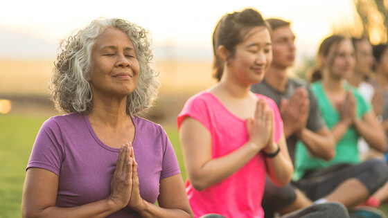 A multi-ethnic group of people meditate during an outdoor yoga class.