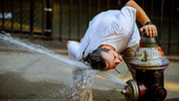 A man inspects a fire hydrant and gets sprayed by it.