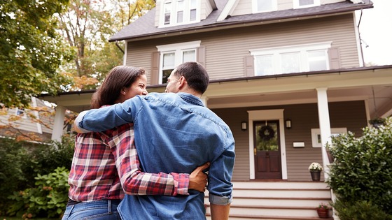 man and woman embrace each other while standing in front of their house 