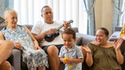 Native Hawaiian family relaxing with a man playing an instrument. 