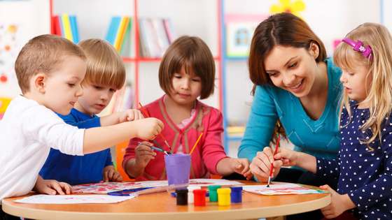 An adult female works with four young children on their paintings.