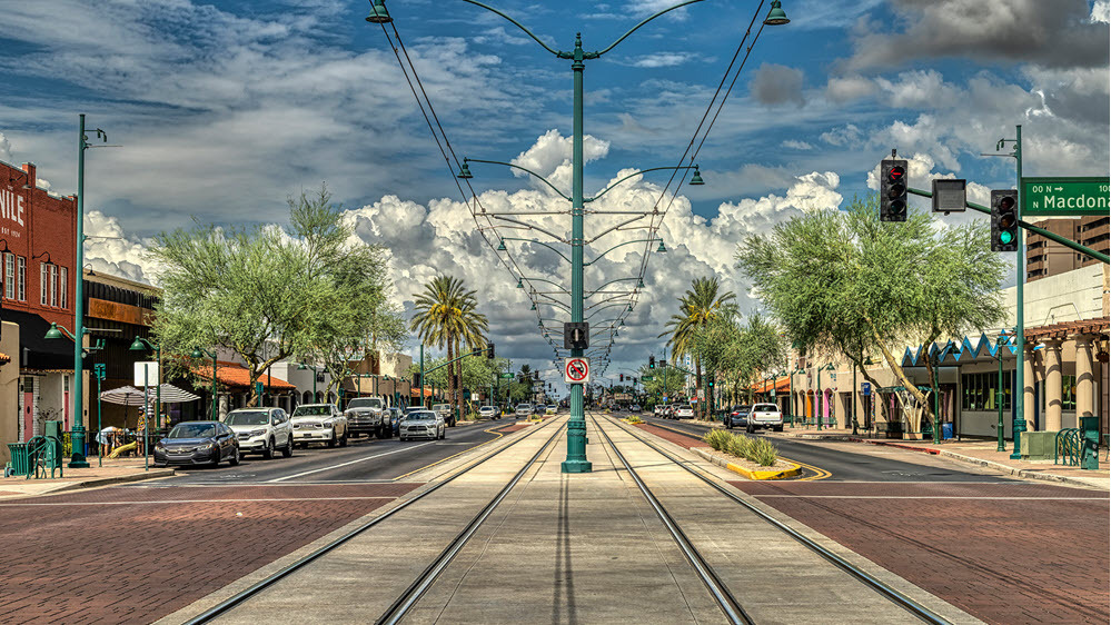 A Mesa, Arizona streetscape with storefronts, trees, and train tracks