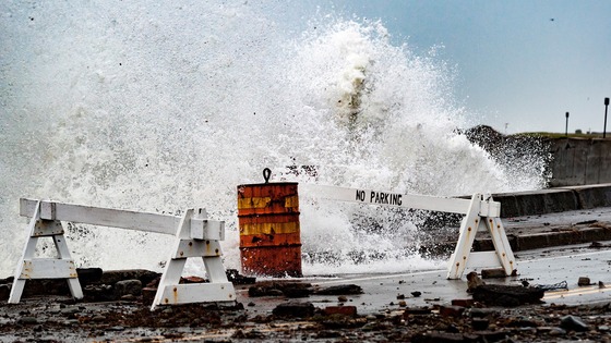 A rogue wave crashes through barriers onto a street.